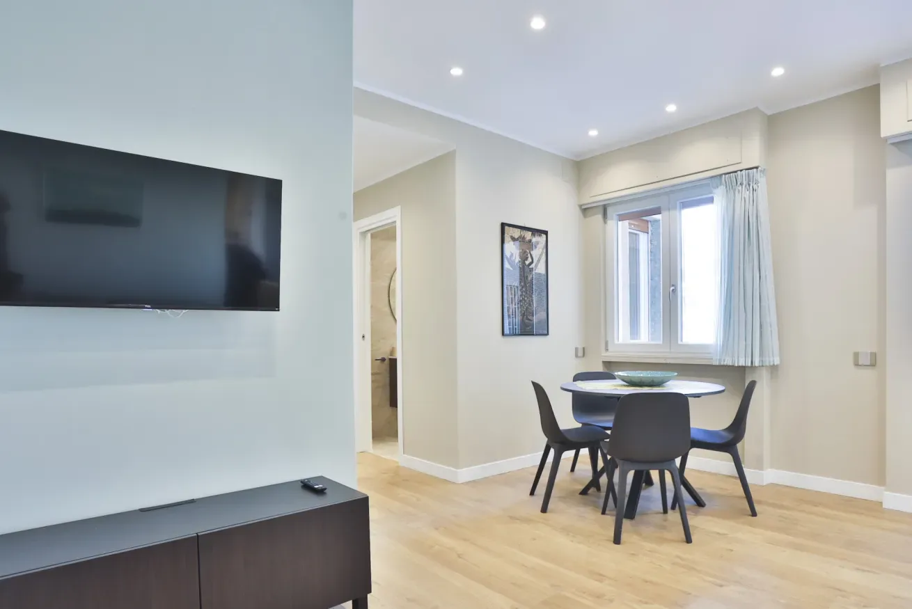 A bright dining area with a round table and wall-mounted television.