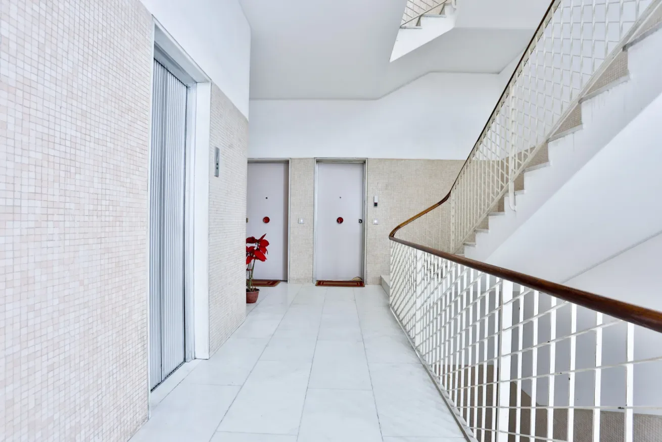 A bright tiled hallway with an elevator and a staircase.