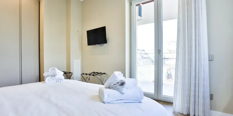 A bedroom with a bed, wall-mounted television, and glass doors opening to a balcony.