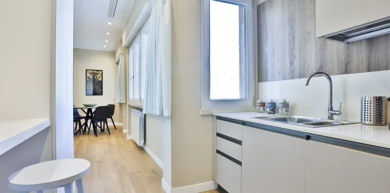A bright kitchen opens onto a narrow dining area with a table and chairs.