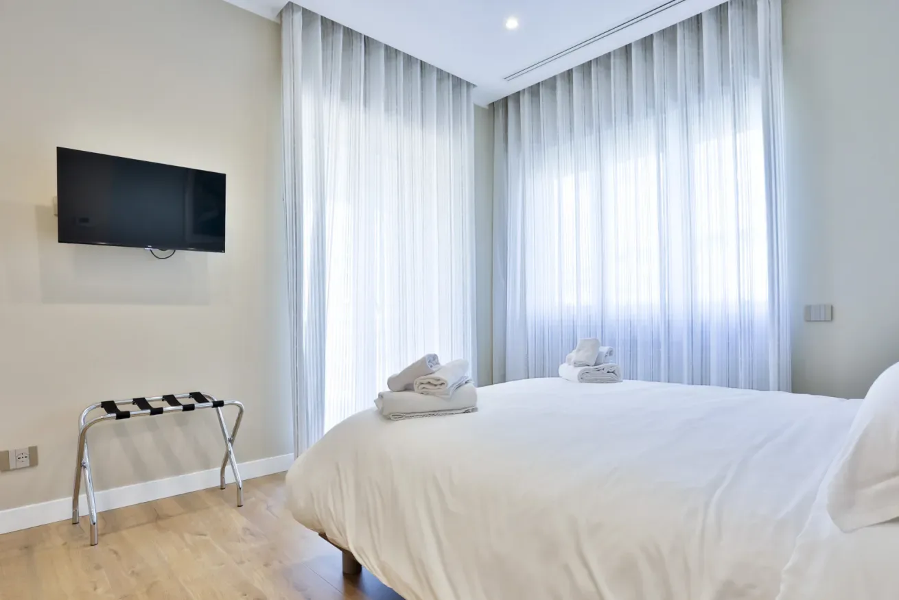 A bright bedroom with a neatly made bed and sheer curtains.