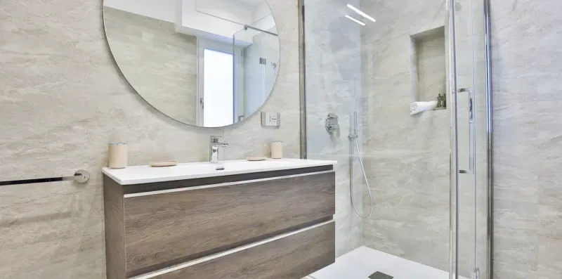 A modern bathroom with a vanity, round mirror, and glass shower.
