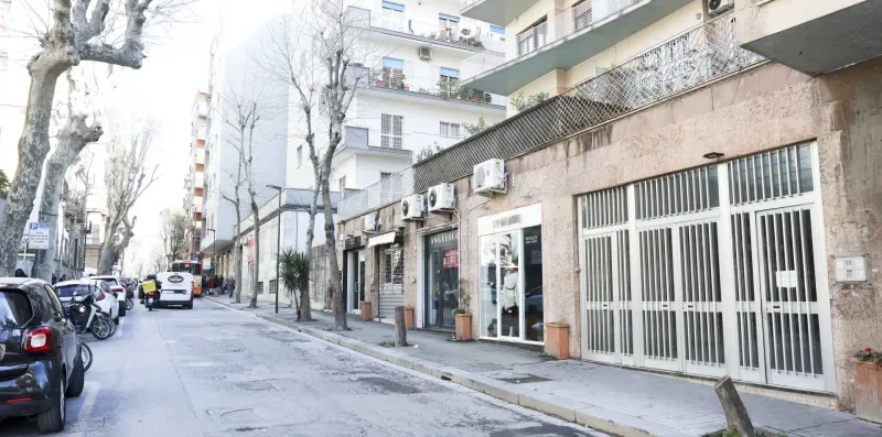 A city street lined with buildings, parked cars, and bare trees.