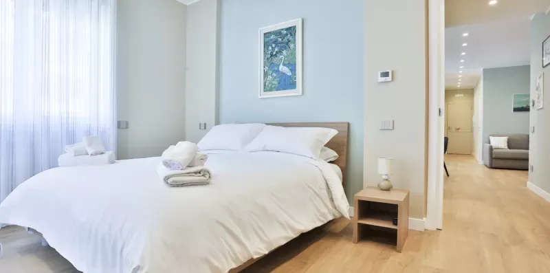 A bright bedroom with a neatly made bed and an open doorway.