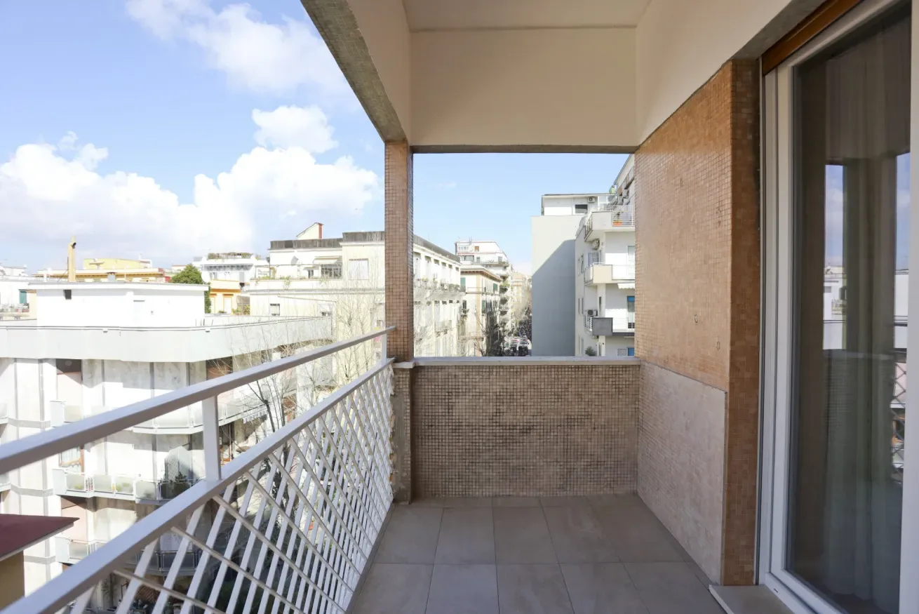 A covered balcony with tiled flooring and views of neighboring buildings.