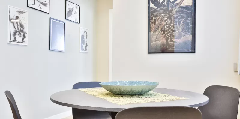 A dining table with a decorative bowl sits beneath framed wall art.