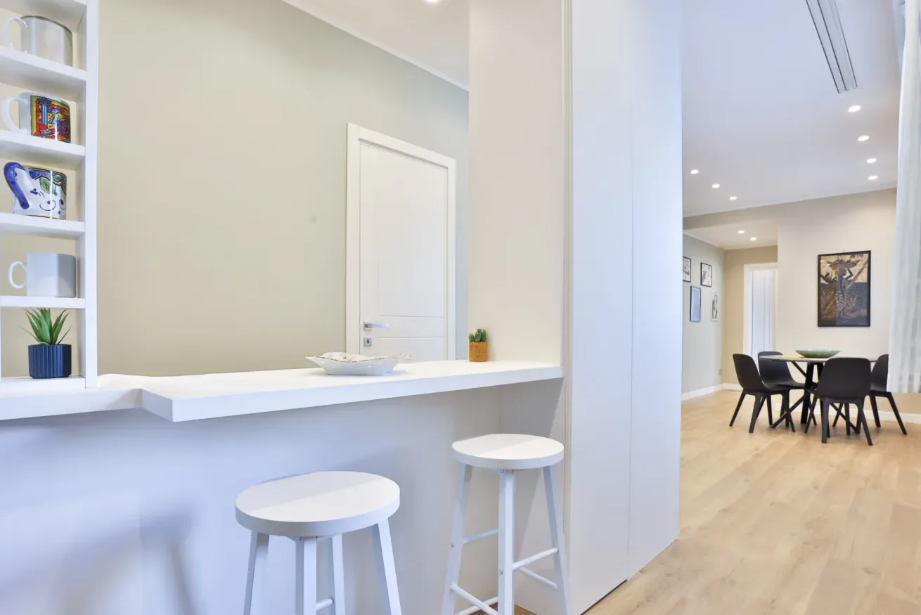 A bright open-plan dining area with a table and stools beside a white counter.