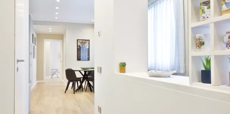 A bright dining area opens onto a hallway, with a table and built-in shelves.