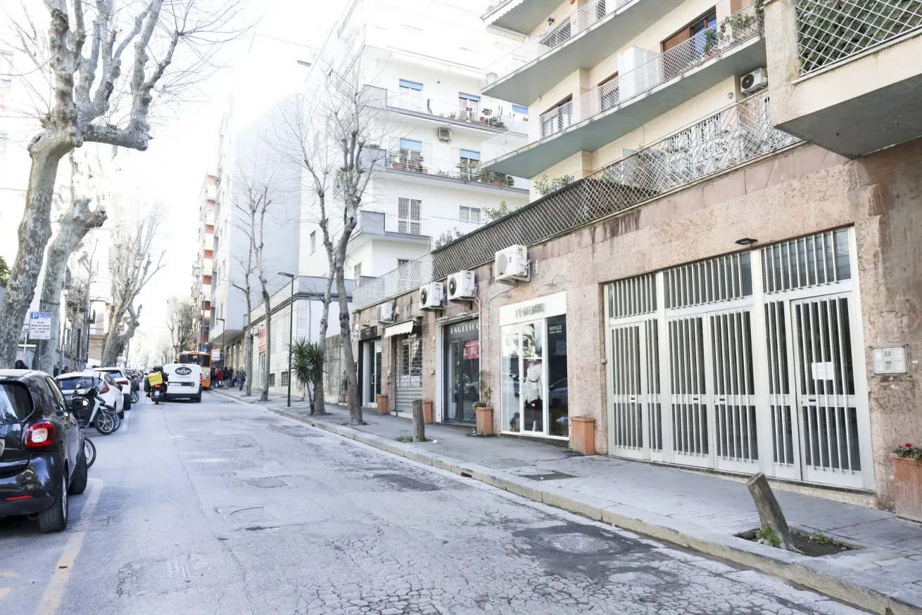 A quiet urban street lined with apartment buildings, storefronts, and parked vehicles.