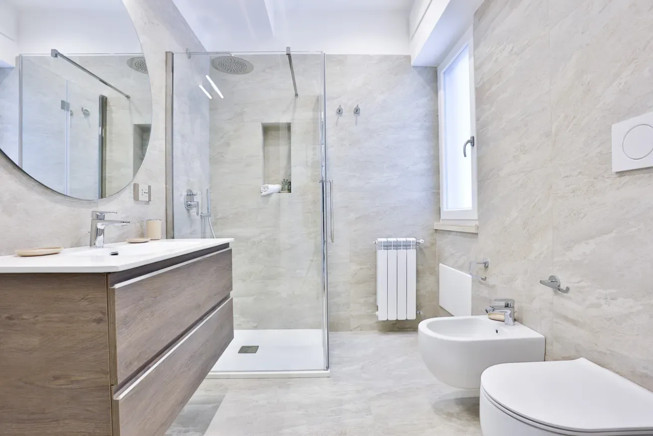 A bright bathroom with a glass shower, vanity, and white fixtures.