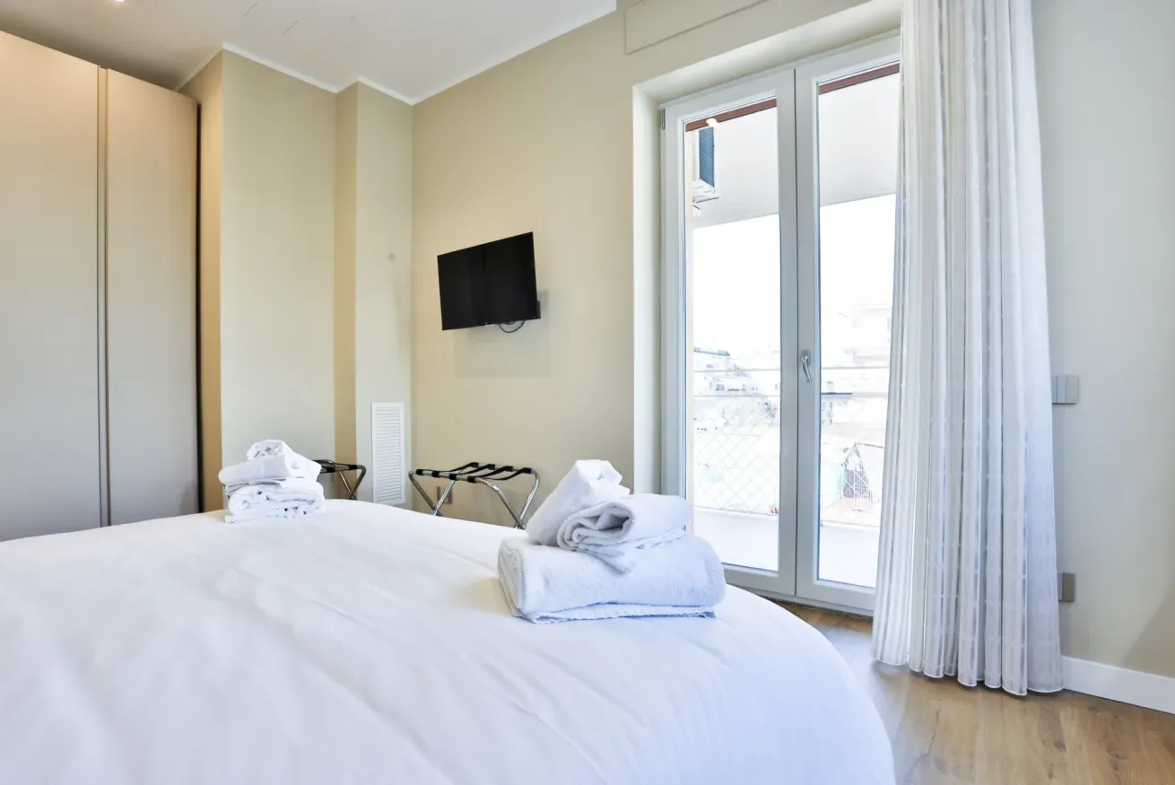 A bedroom with a bed, folded towels, and a television mounted on the wall.