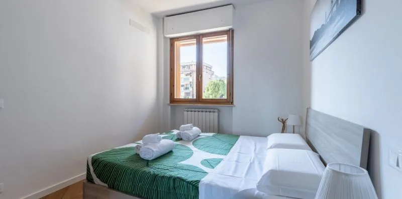 A bedroom with a bed dressed in green and white linens beneath a window.
