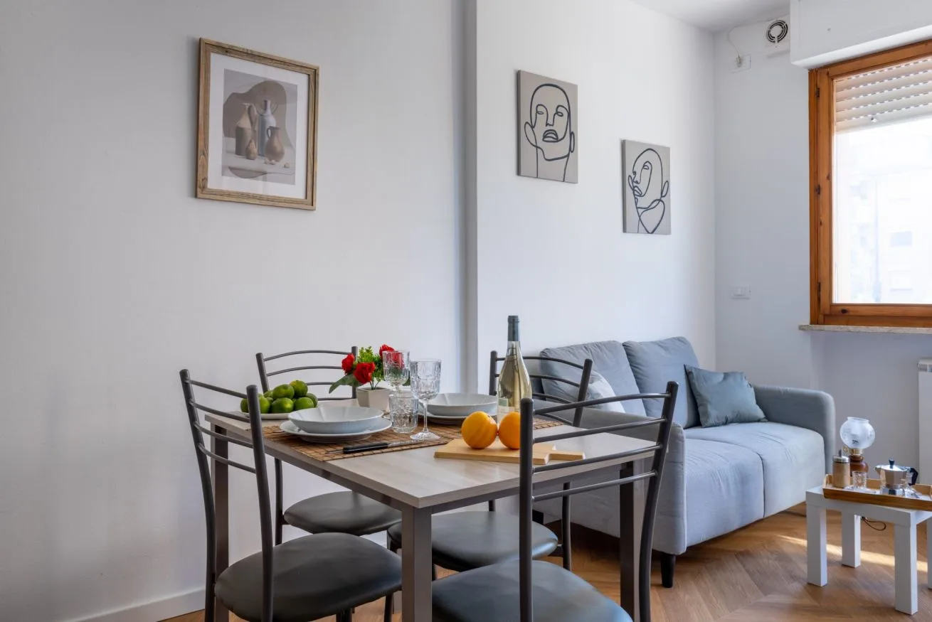 A dining table with chairs sits beside a sofa in a bright living room.
