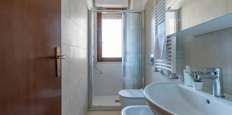 A tiled bathroom with a shower, sink, and wall-mounted towel warmer.