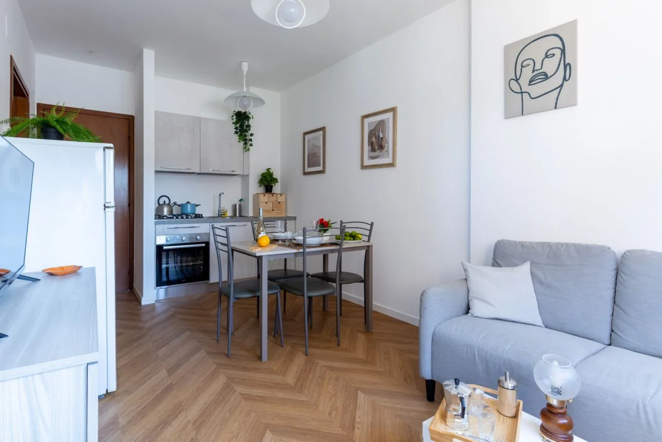 A bright living and dining area opens onto a compact kitchen, with a gray sofa.