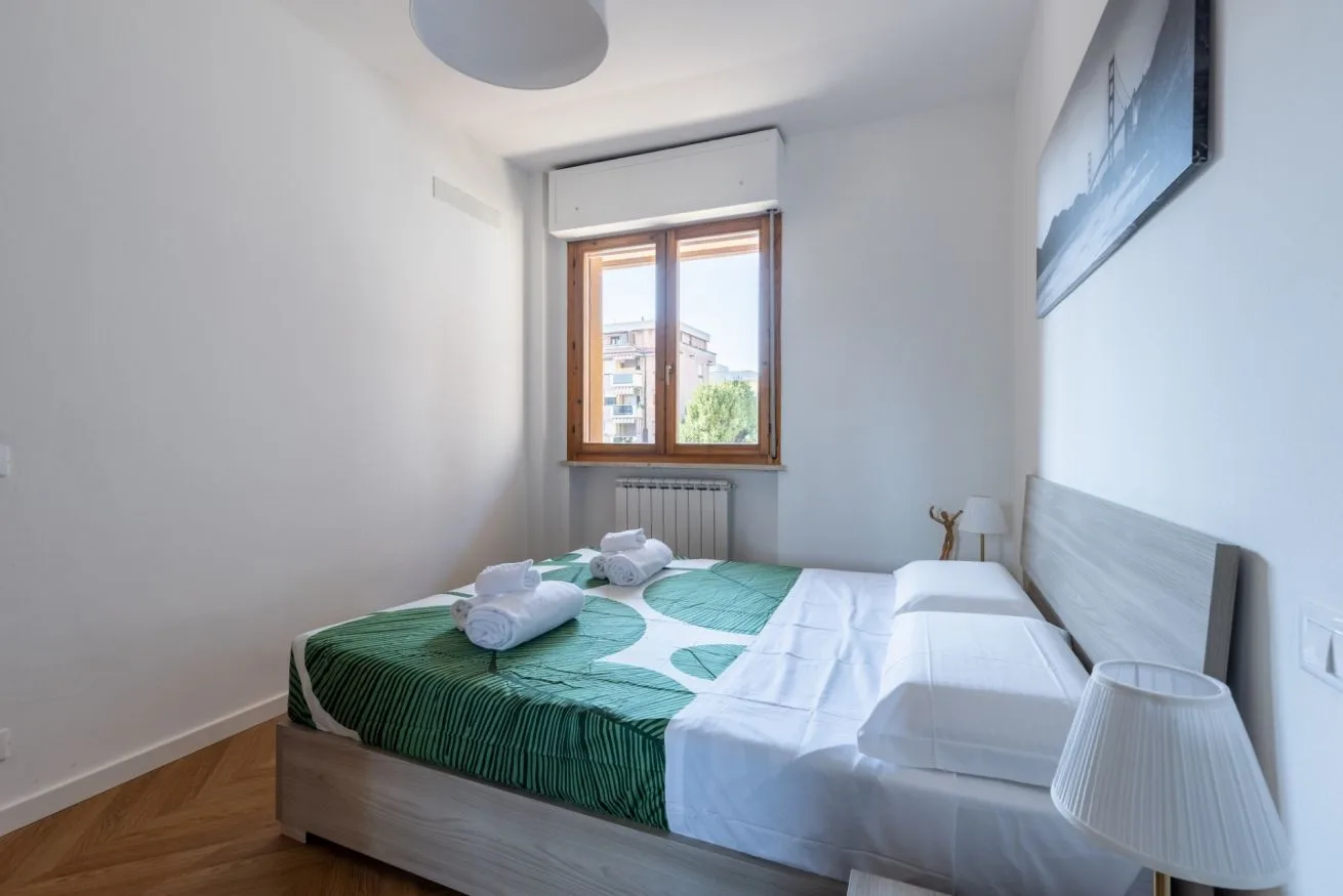 A bedroom with a bed dressed in green and white bedding beneath a window.