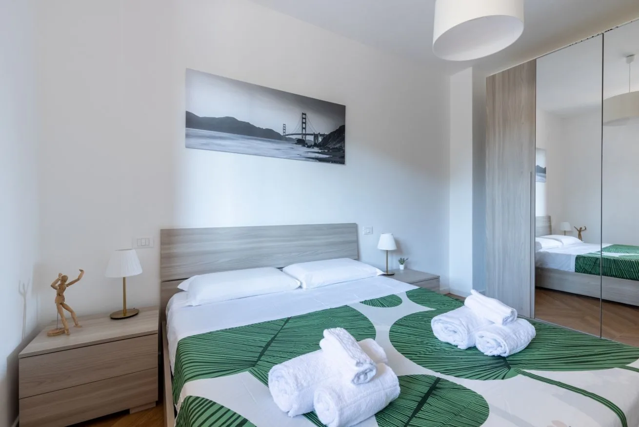 A bright bedroom with a bed dressed in white and green linens.