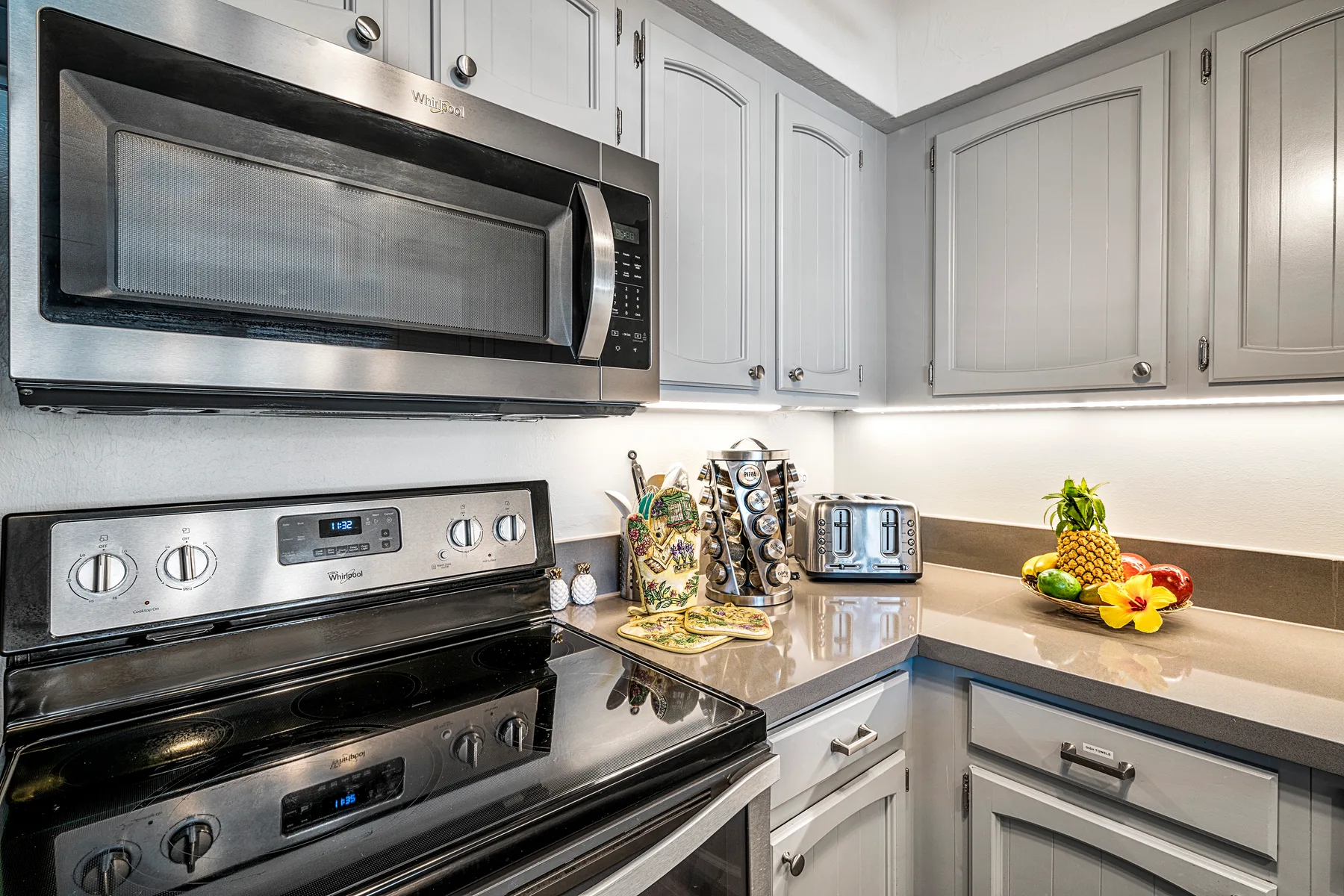 A bright kitchen with white cabinets, a stainless microwave, and a stove.