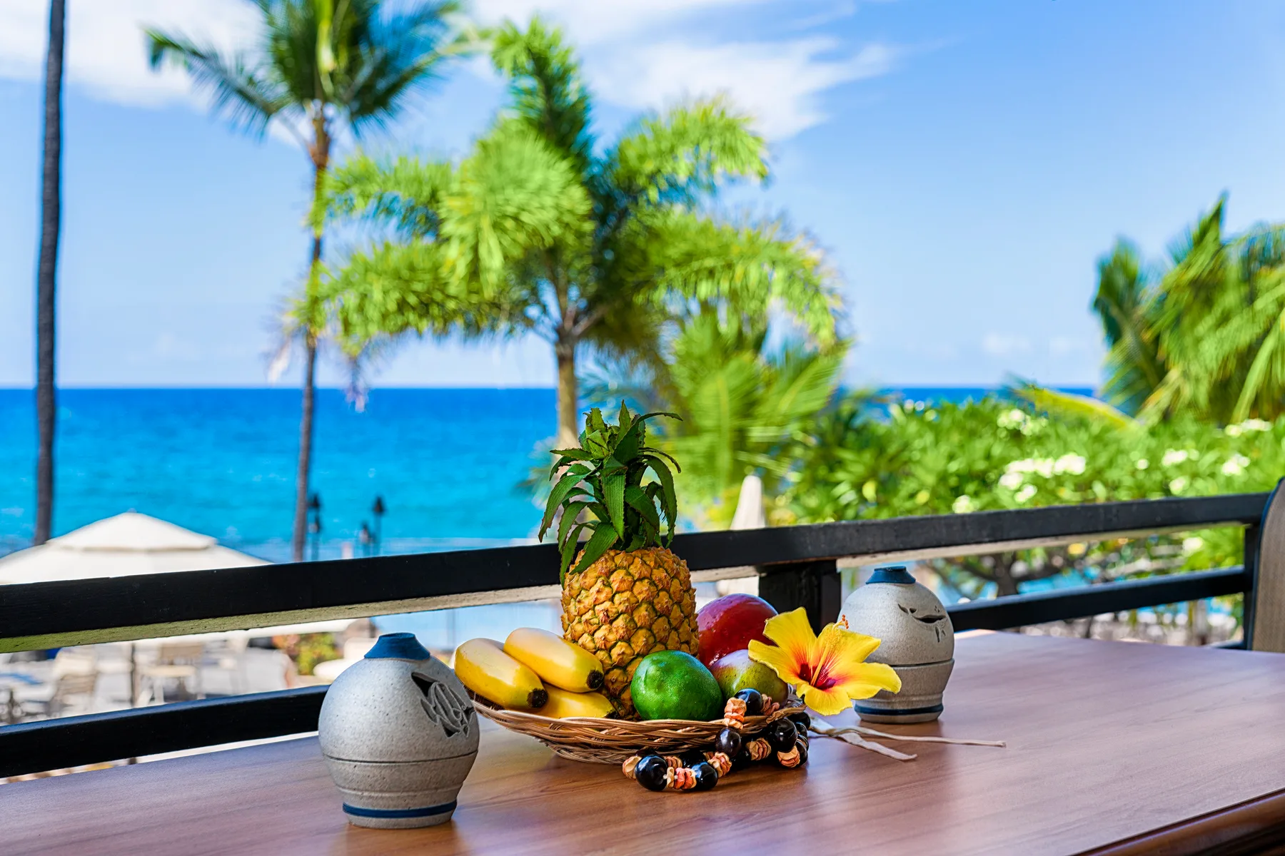 A tropical seaside view with fruit arranged on a table beside the railing.