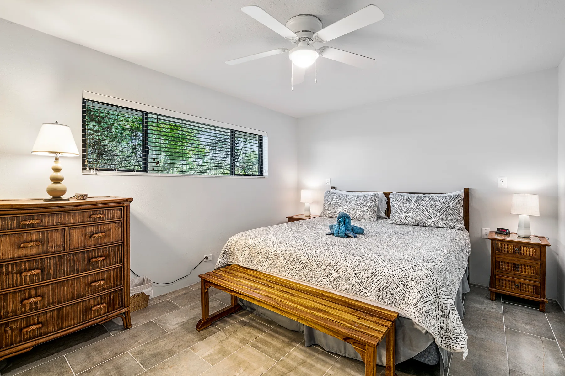 A bedroom with a bed, wooden bench, and window with blinds.