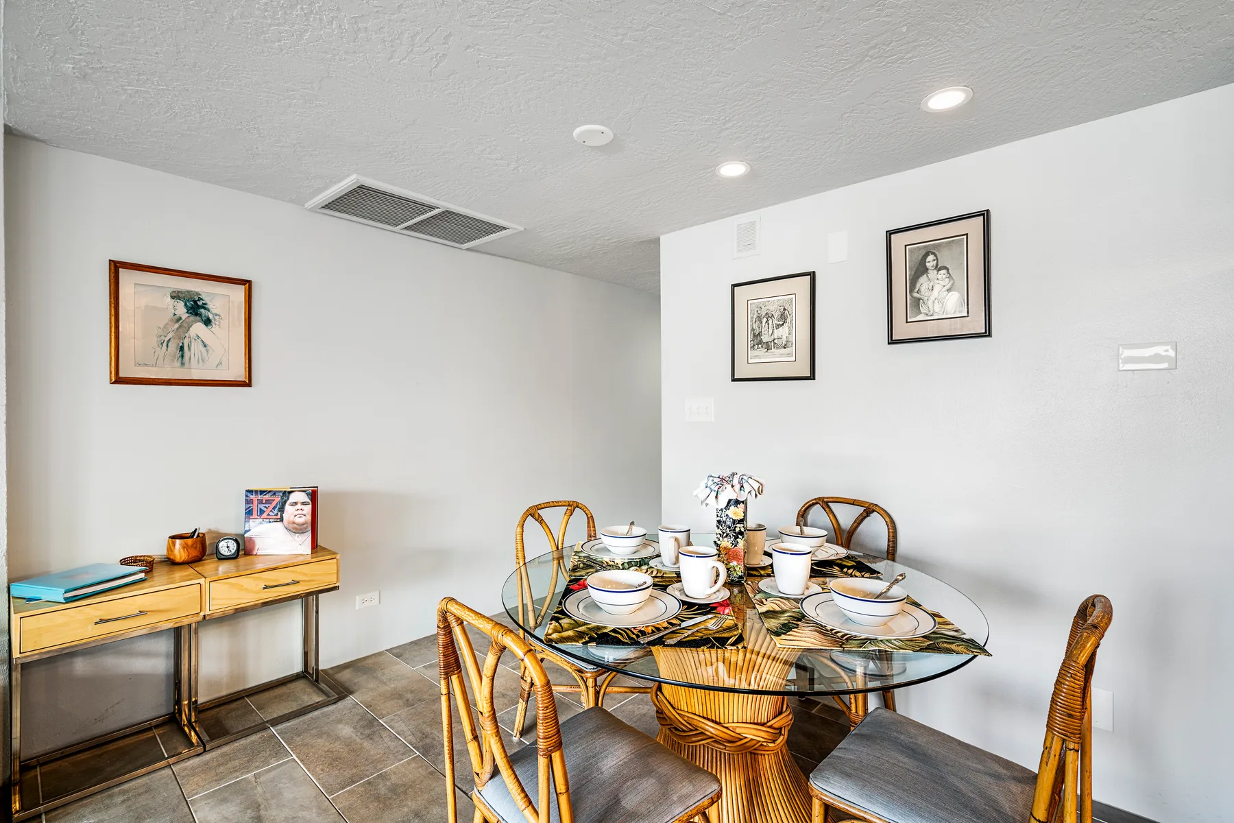 A dining area with a round glass table, woven seating, and framed artwork.