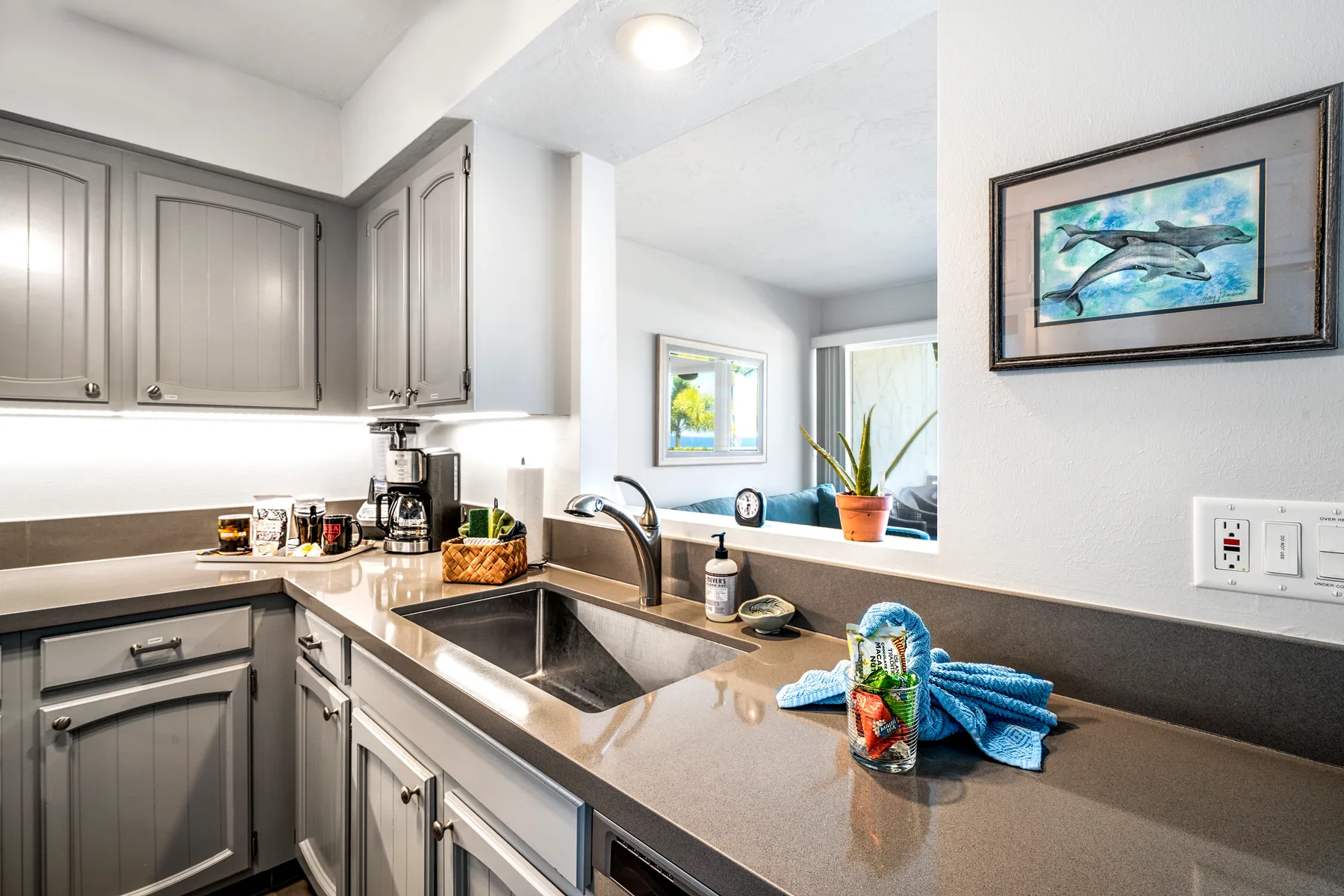 A bright kitchen with gray cabinets, a sink, and a long countertop.
