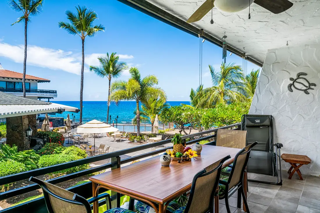 A covered patio dining area overlooks palm trees and the ocean.