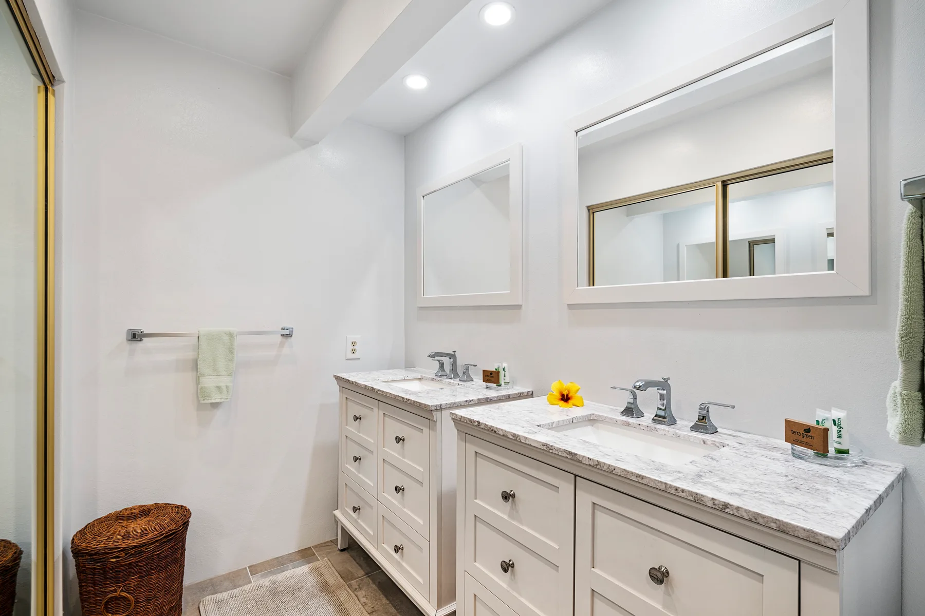 A bright bathroom with a long vanity, mirrors, and a towel rack.