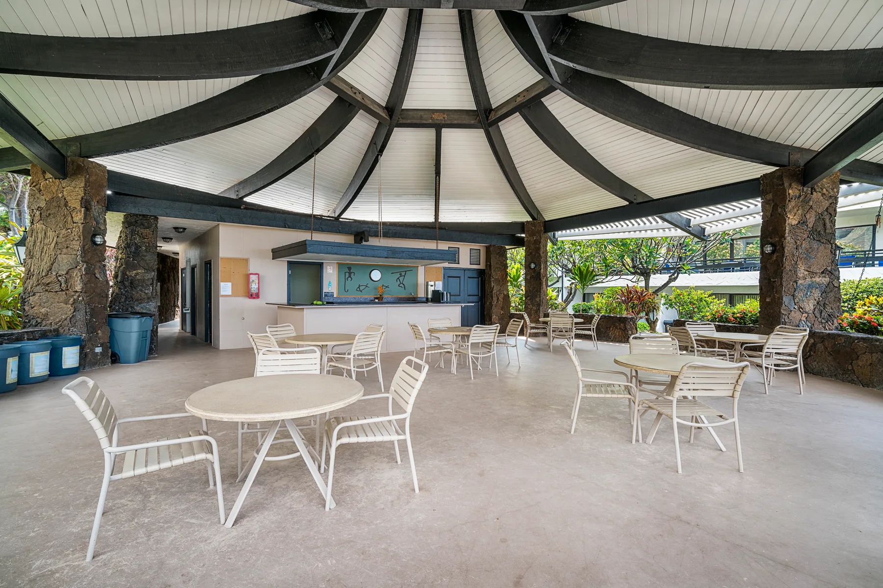An open-air dining area with white tables and seating beneath a curved roof.
