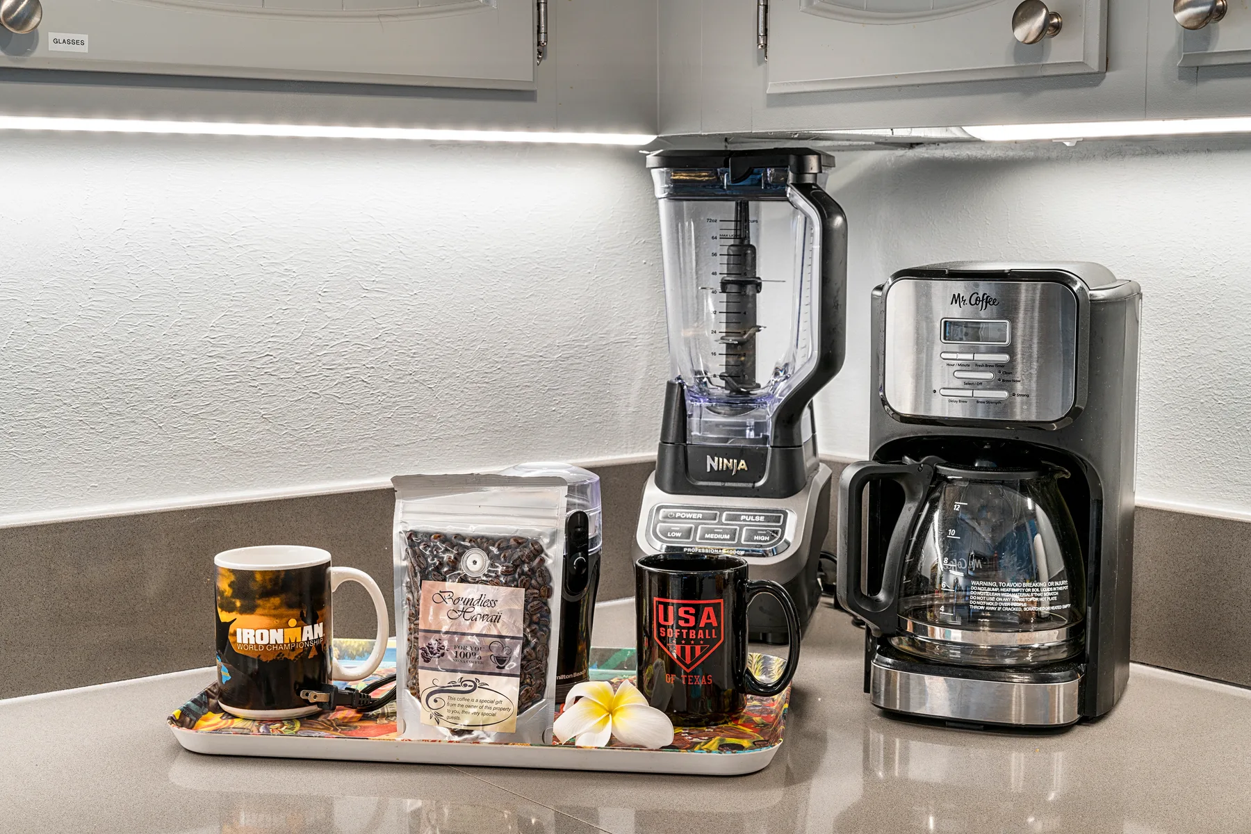 A kitchen counter displays a blender, coffee maker, and a tray of mugs.