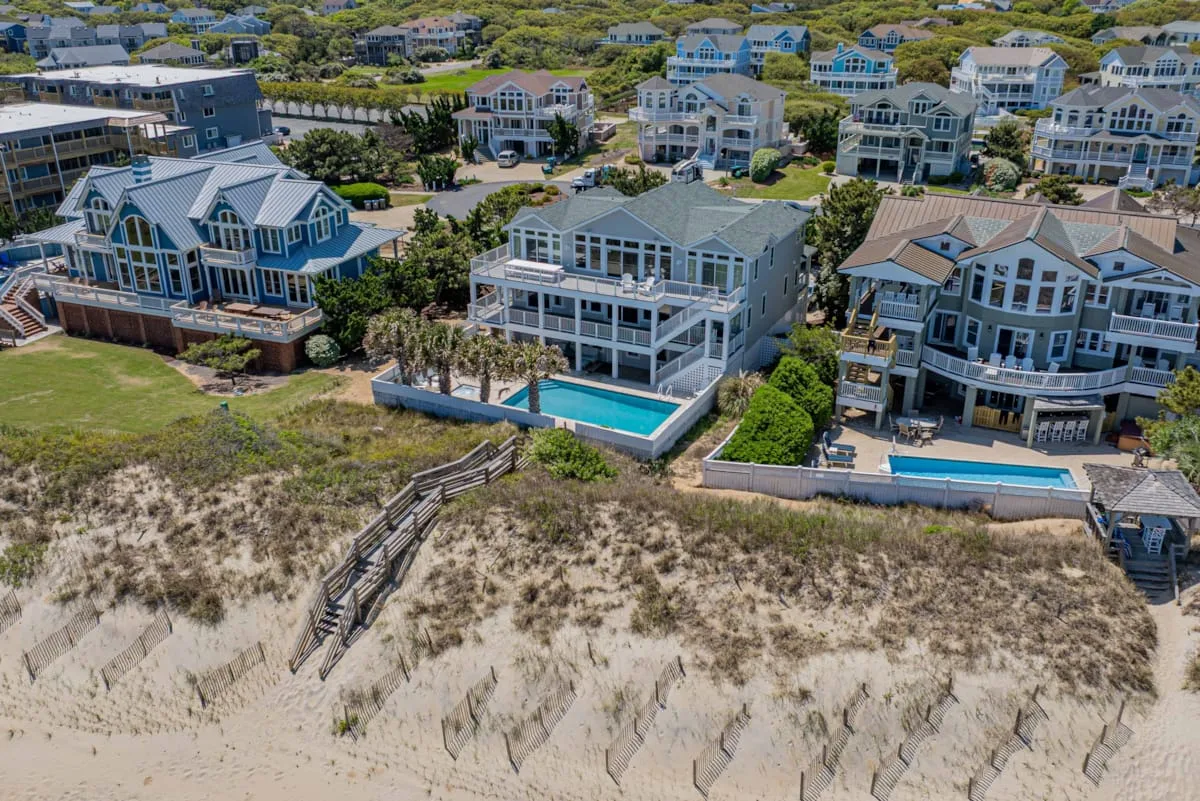 Aerial view of coastal houses with swimming pools beside a sandy beach.