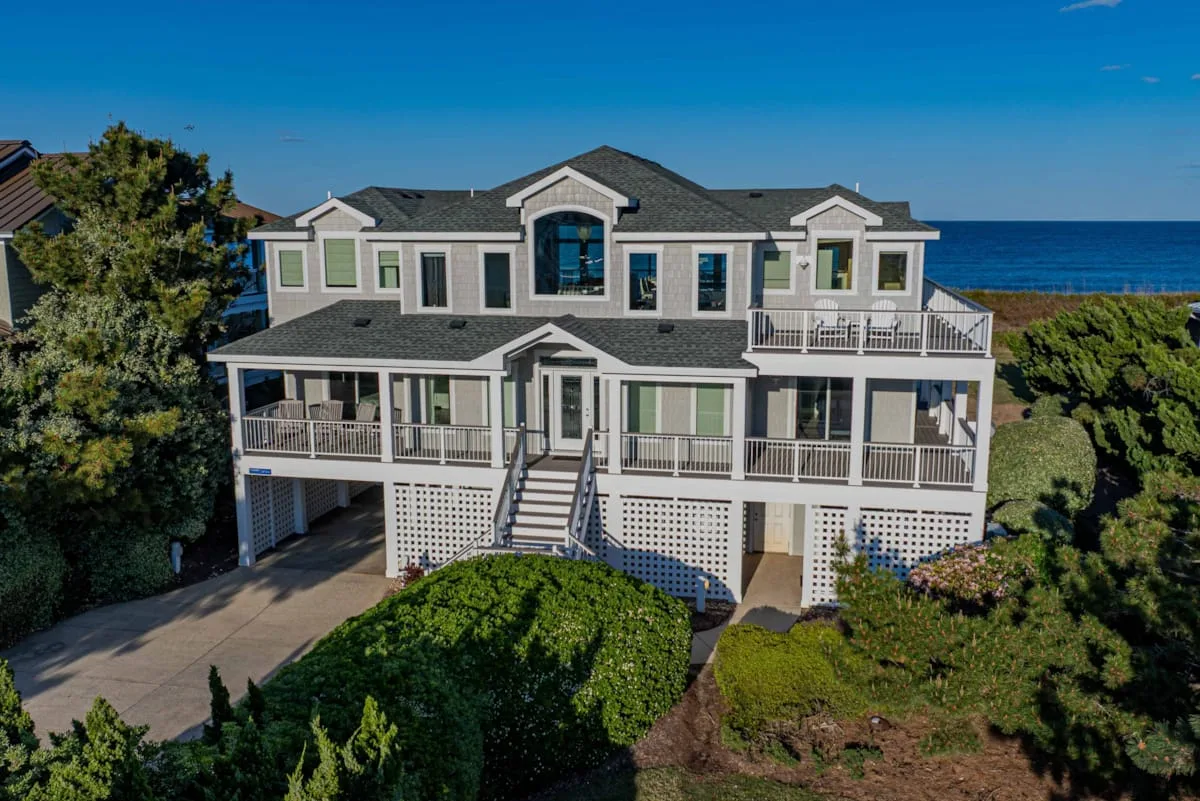 A large coastal house with multiple balconies stands beside the ocean.