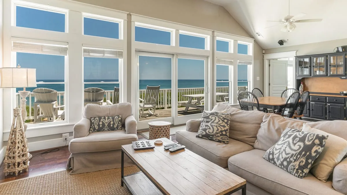 A bright living room with seating and large windows overlooking the ocean.