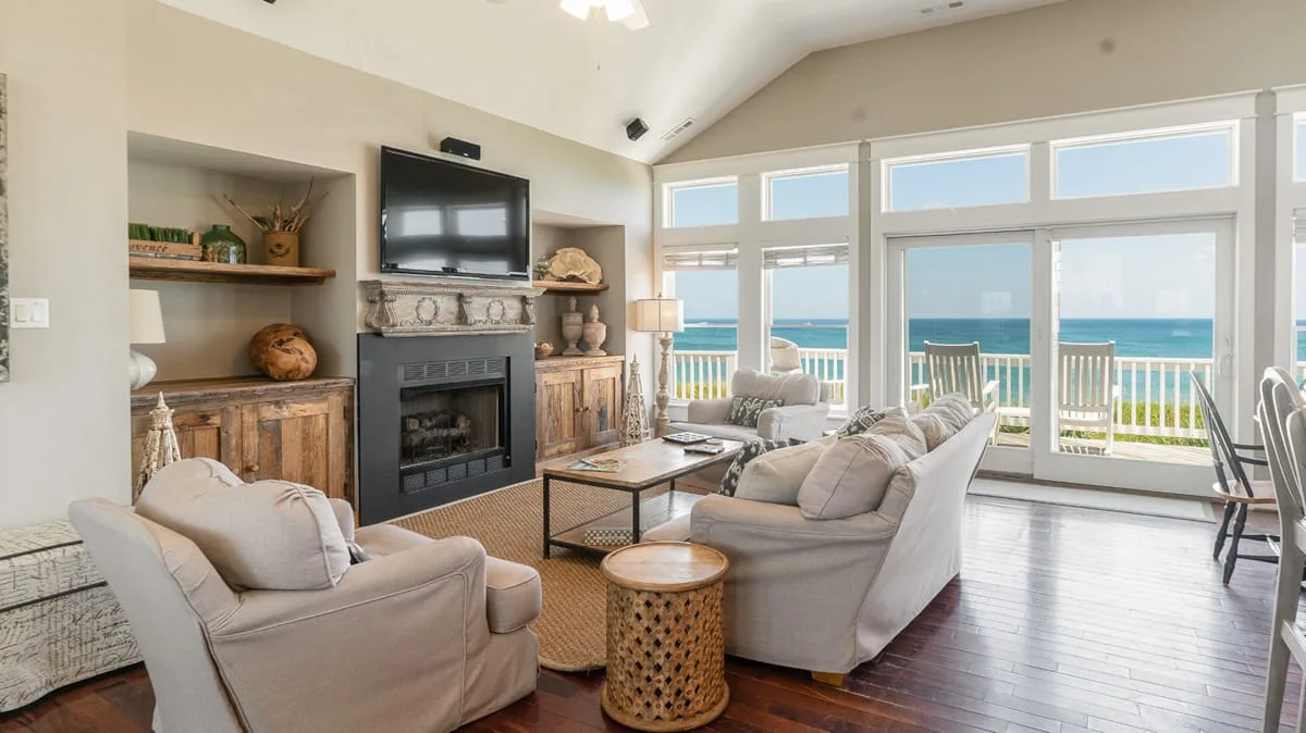 A bright living room with seating, a fireplace, and large windows overlooking the ocean.