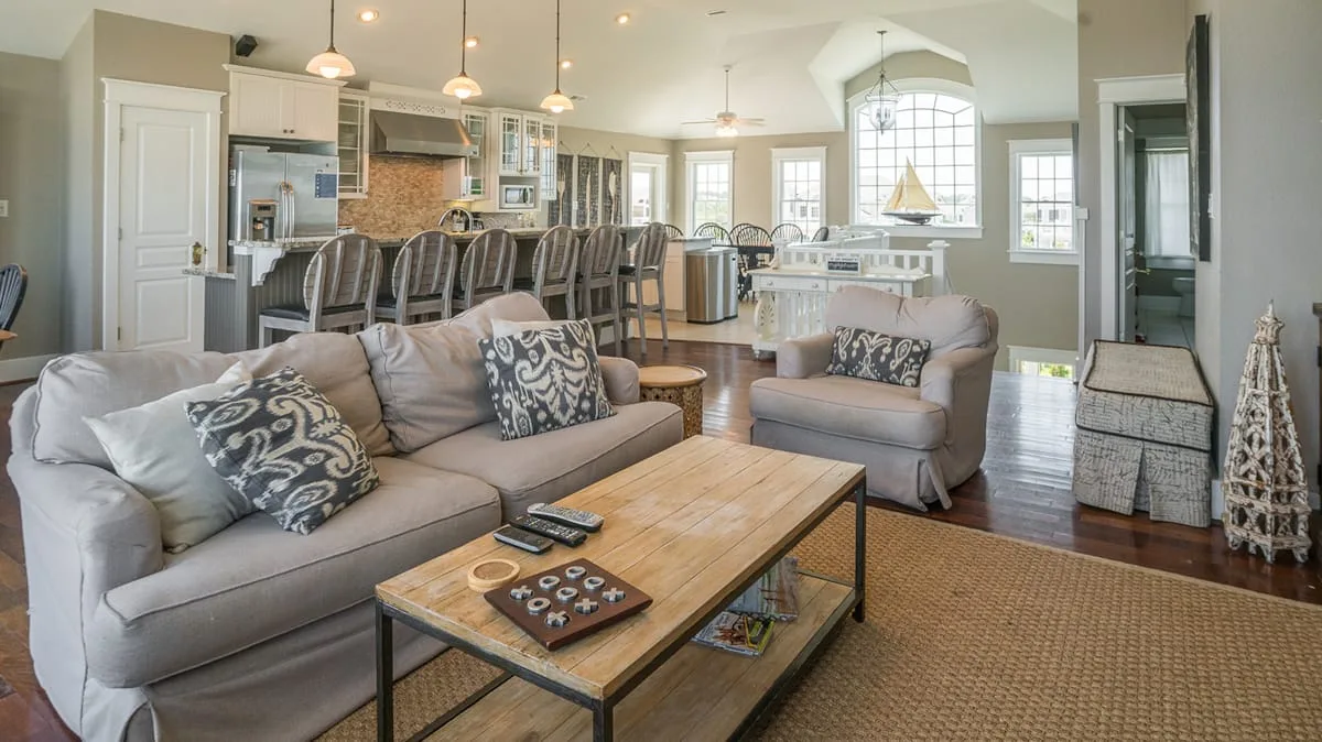 A living room with seating around a wooden coffee table, open to a kitchen and dining area.