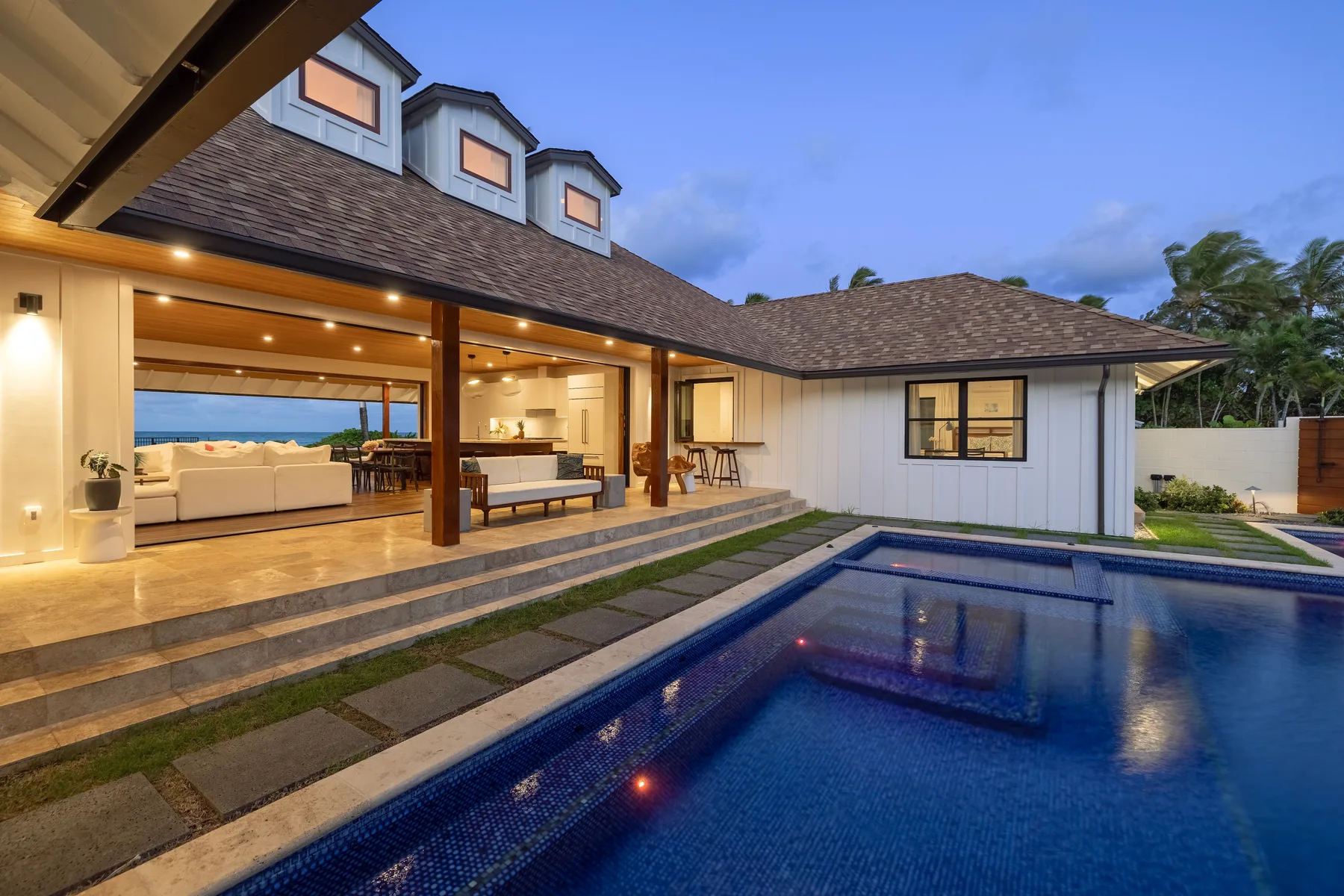 A modern house opens onto a pool, with outdoor seating beneath a covered patio.