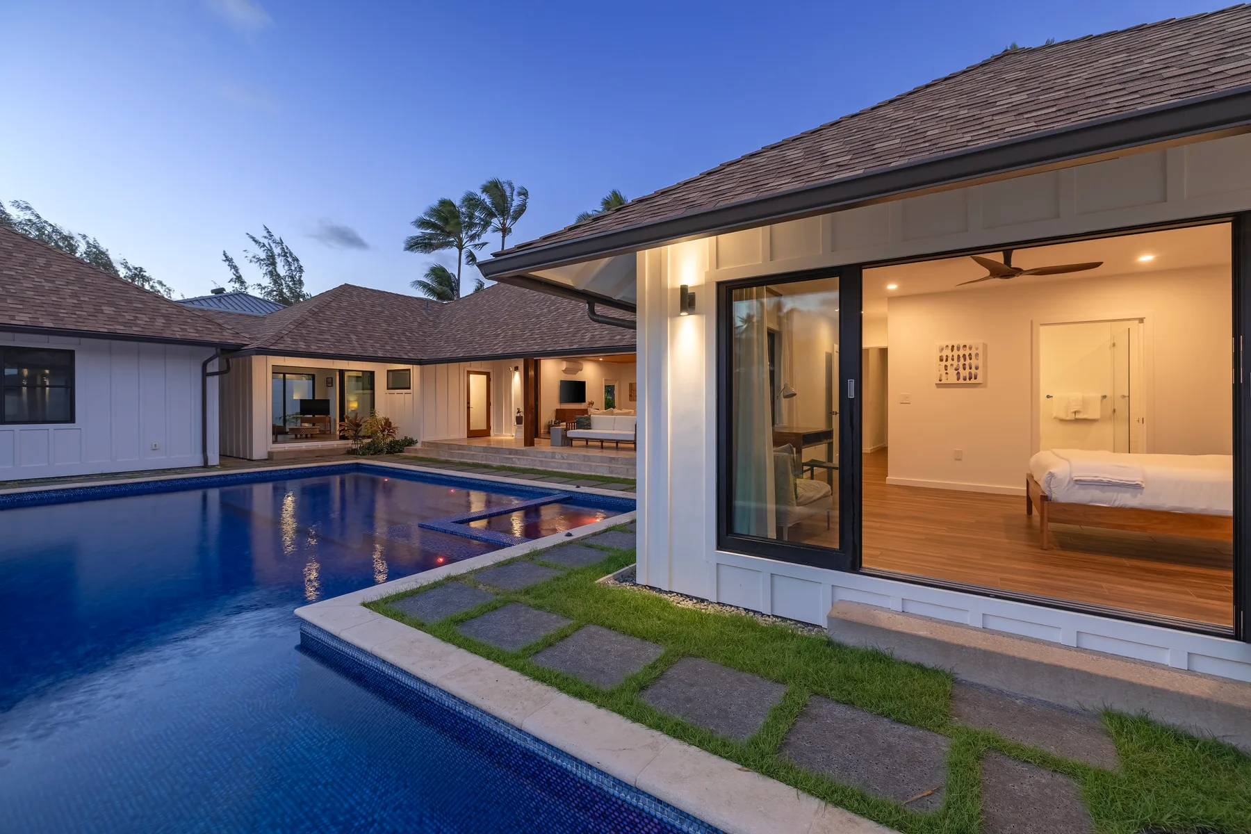 A courtyard pool beside a modern home, with an open bedroom visible through glass doors.