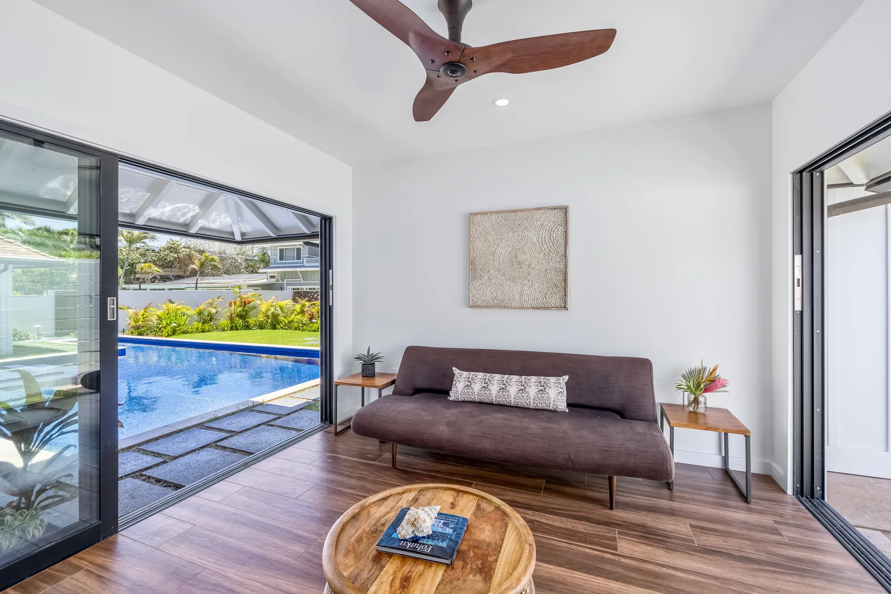 A bright living room with seating beside large sliding glass doors overlooking a pool.