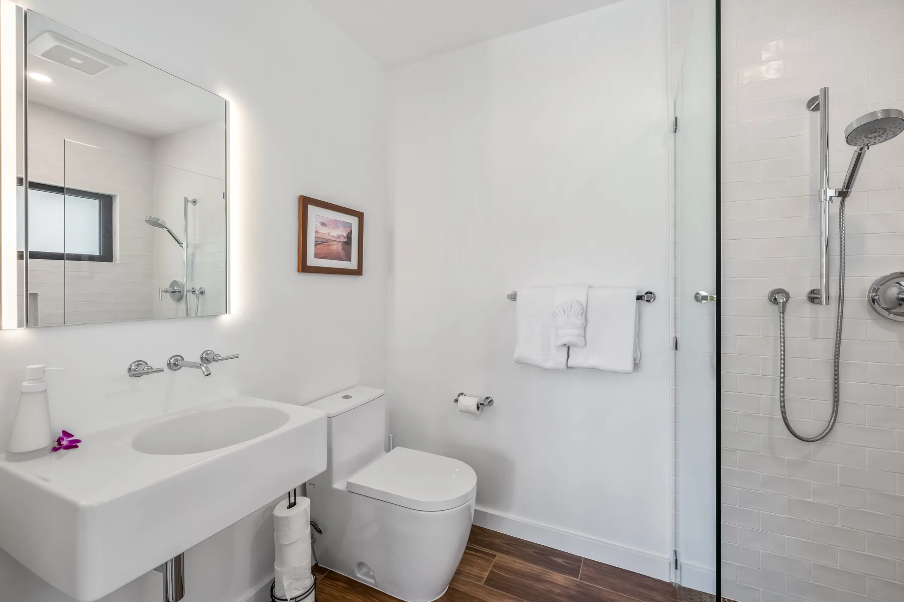 A bright bathroom with a sink, toilet, and glass-enclosed shower.