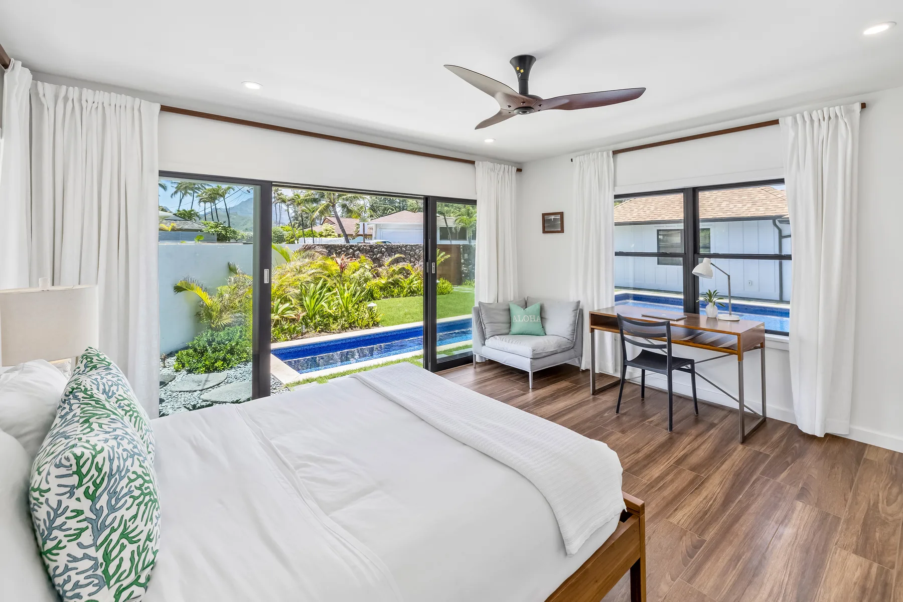 A bright bedroom with a bed, seating, and large windows overlooking a garden.
