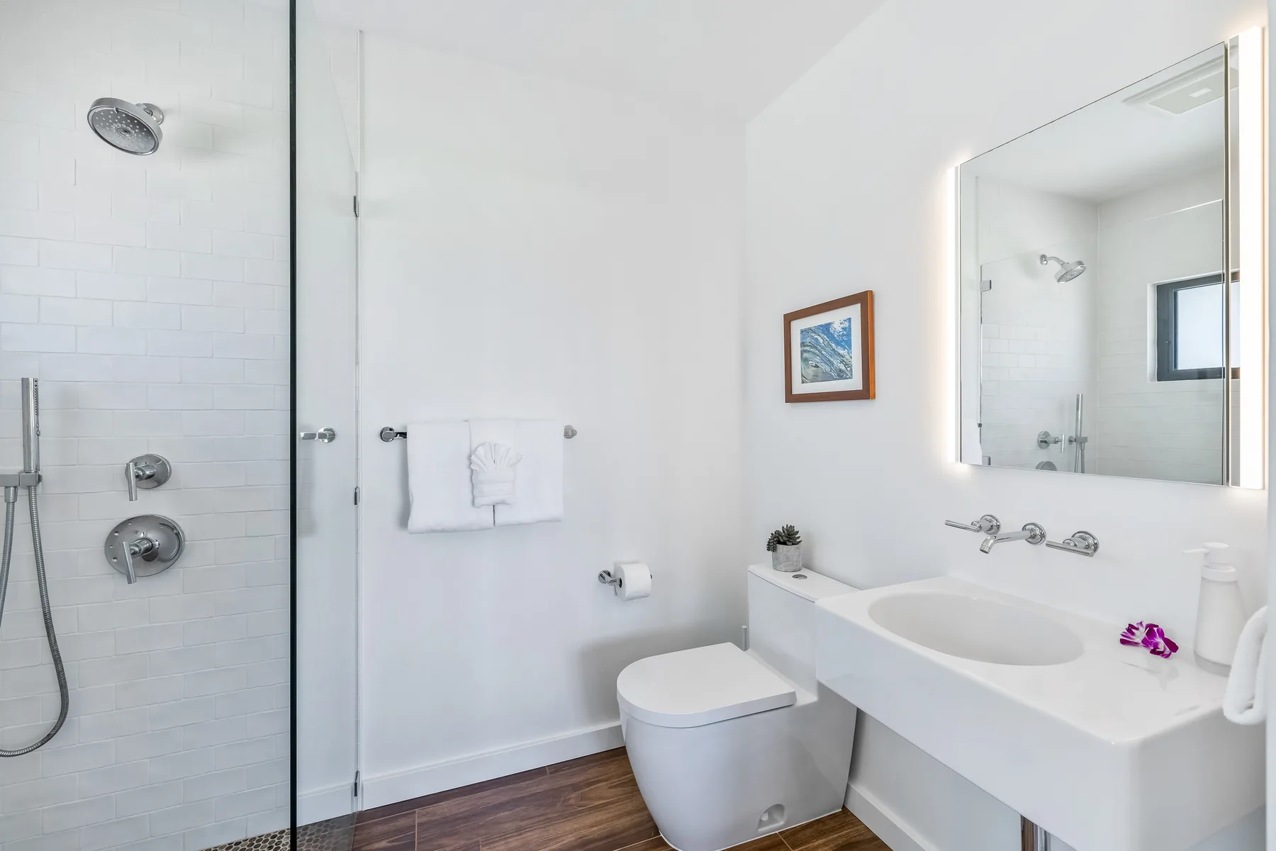 A bright bathroom with a glass shower, toilet, and wide sink counter.