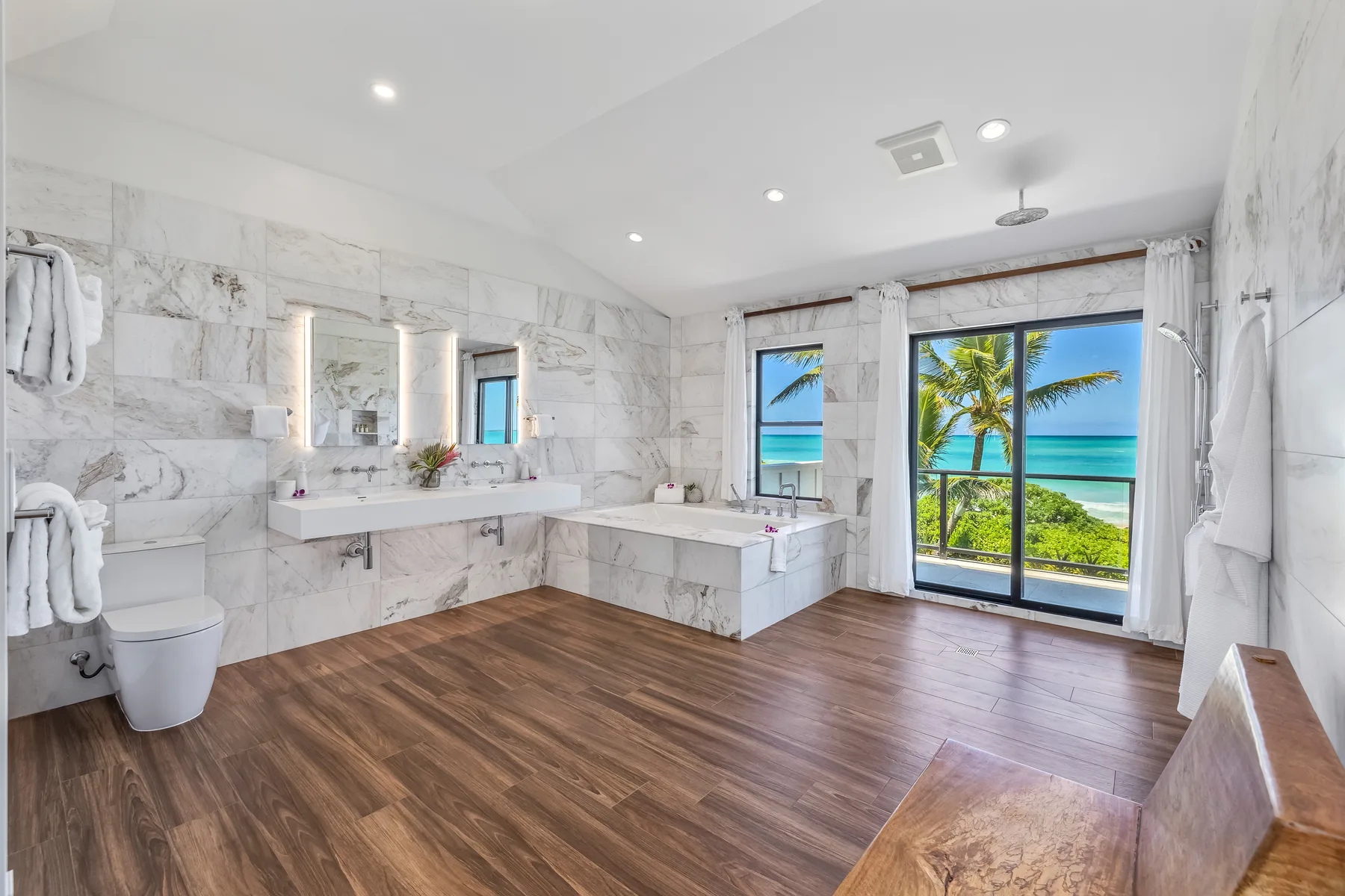 A spacious bathroom with a bathtub, vanity, and ocean views through wide windows.