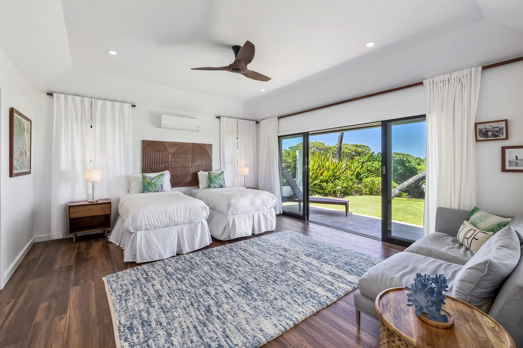A bright bedroom with twin beds and sliding glass doors opening onto a garden.