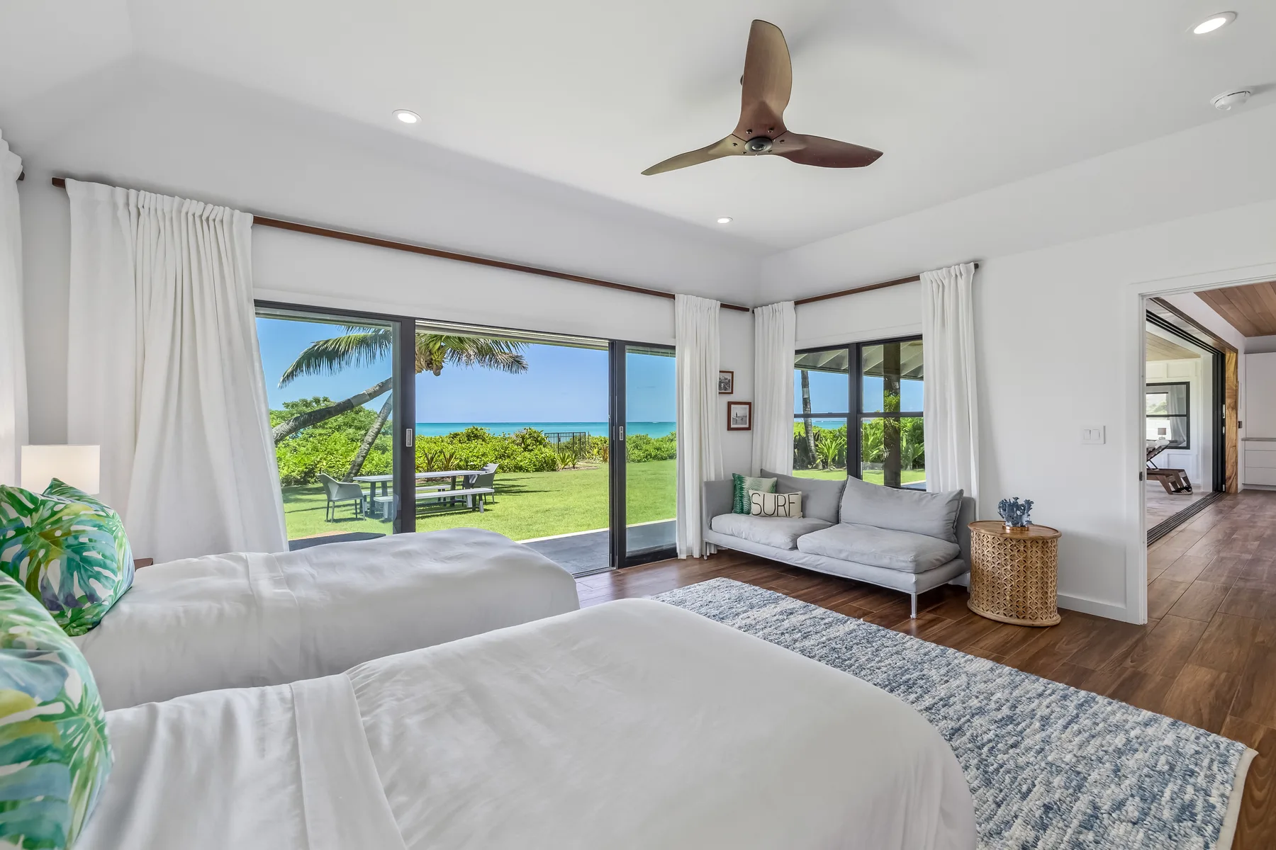 A bright bedroom with beds, a seating area, and views of the ocean.