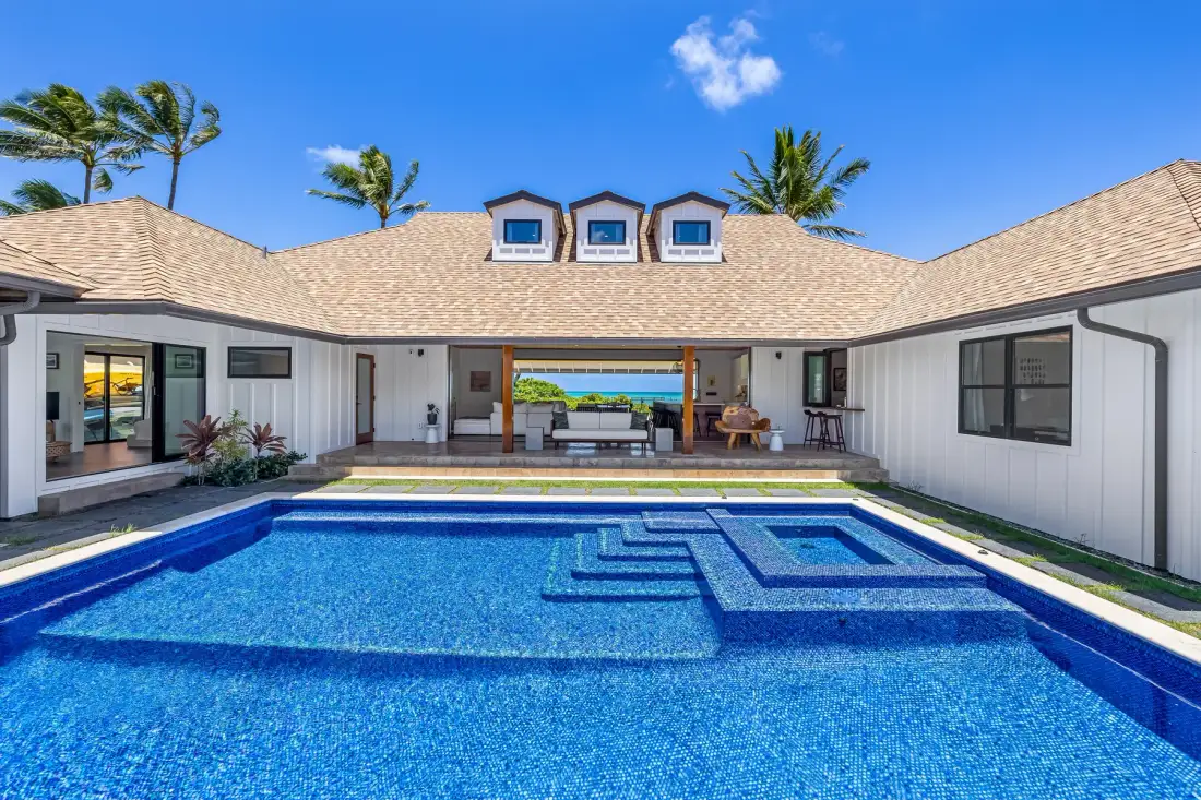 Una piscina frente a una casa blanca con un patio cubierto.