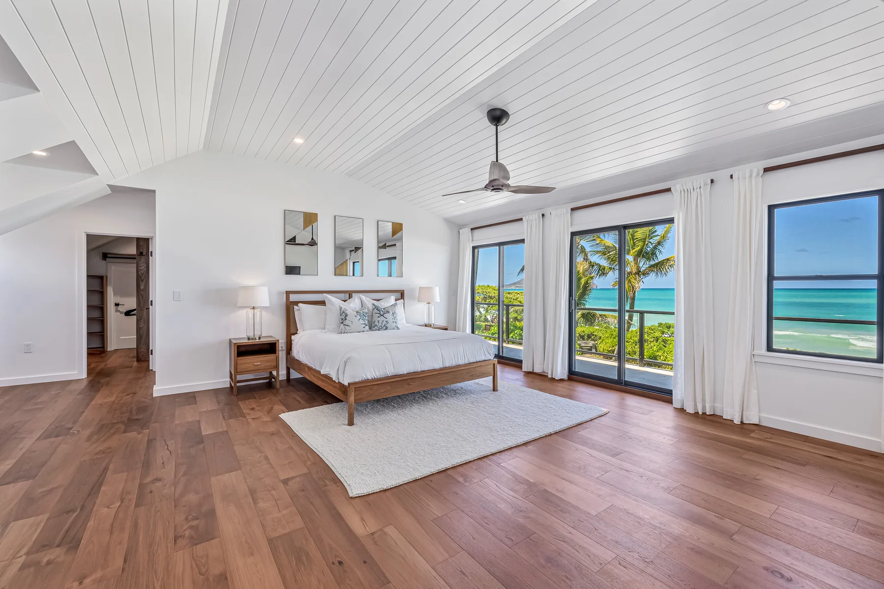 A bright bedroom with a bed and wide windows overlooking the ocean.