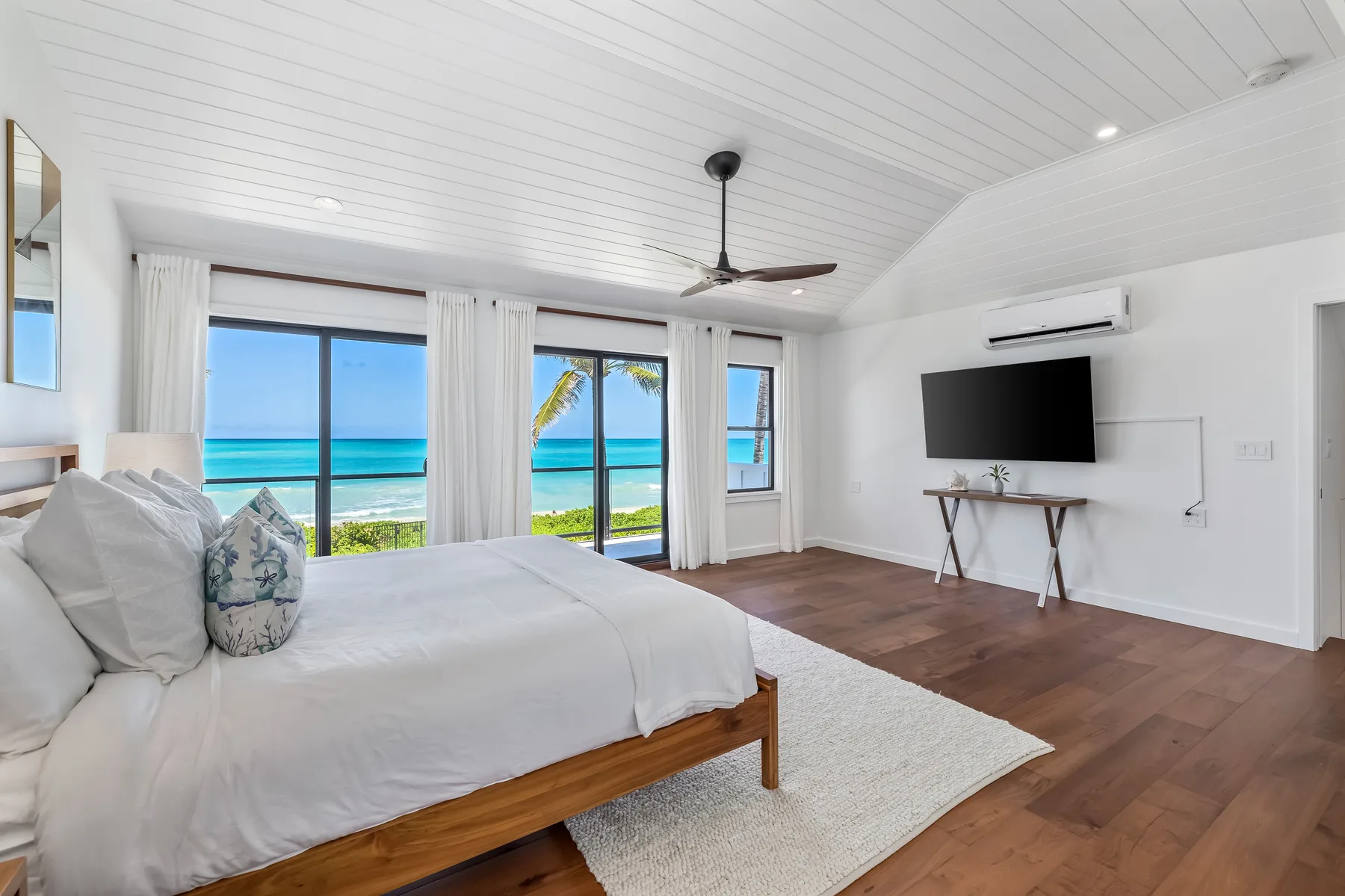 A bedroom with a bed facing large windows overlooking the ocean.