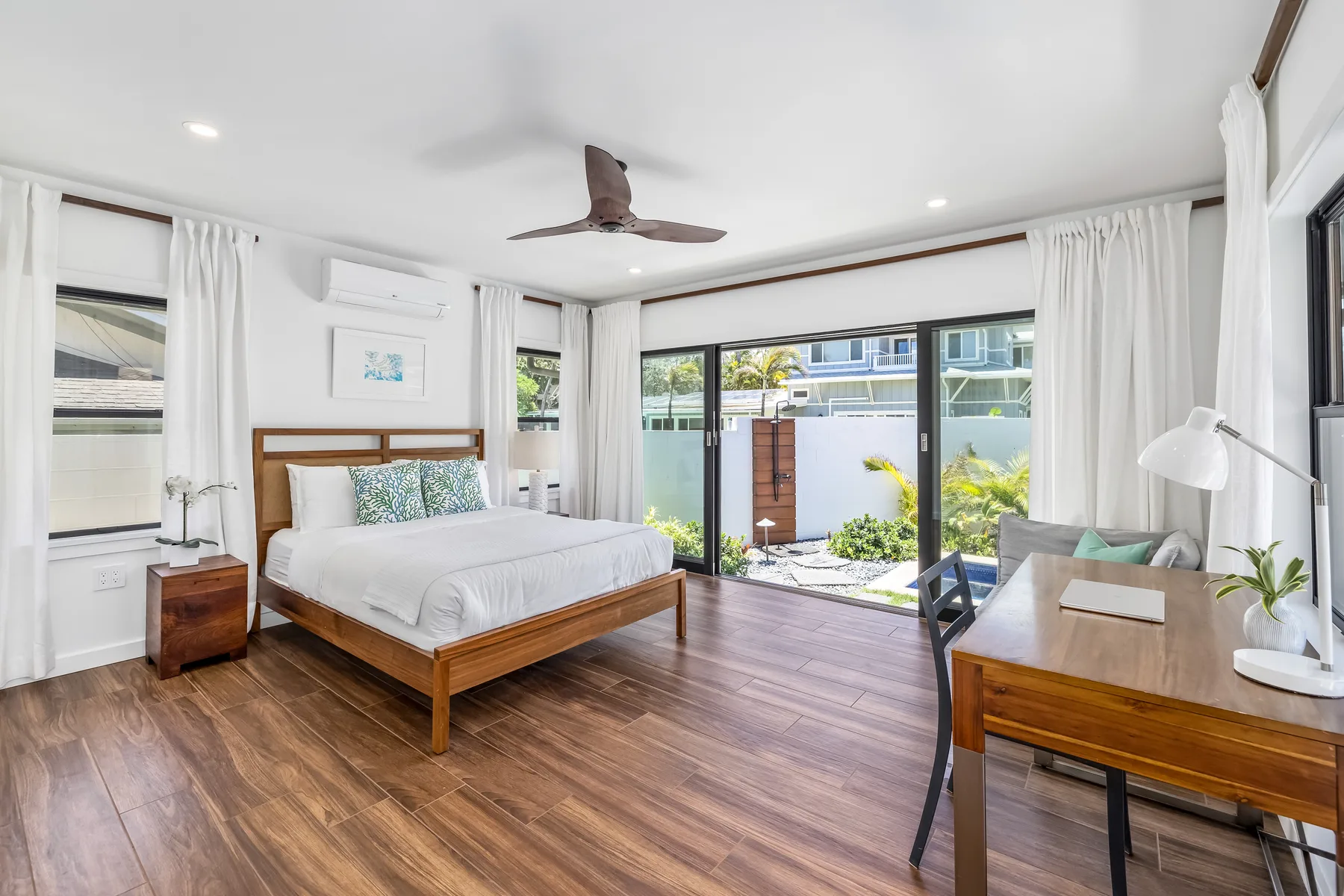 A bright bedroom with a wooden bed and glass doors opening to a patio.