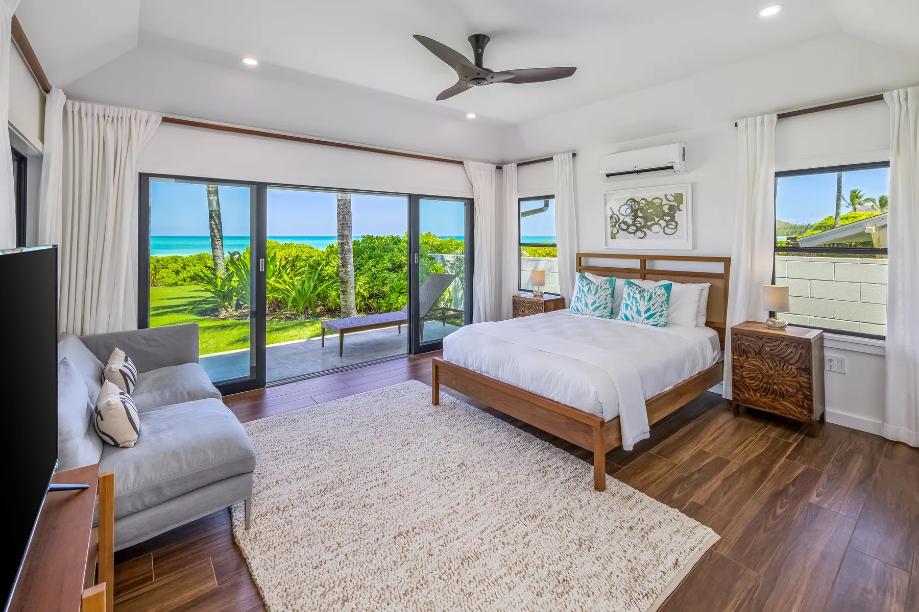 A bright bedroom with a bed, seating, and sliding glass doors opening onto tropical greenery.