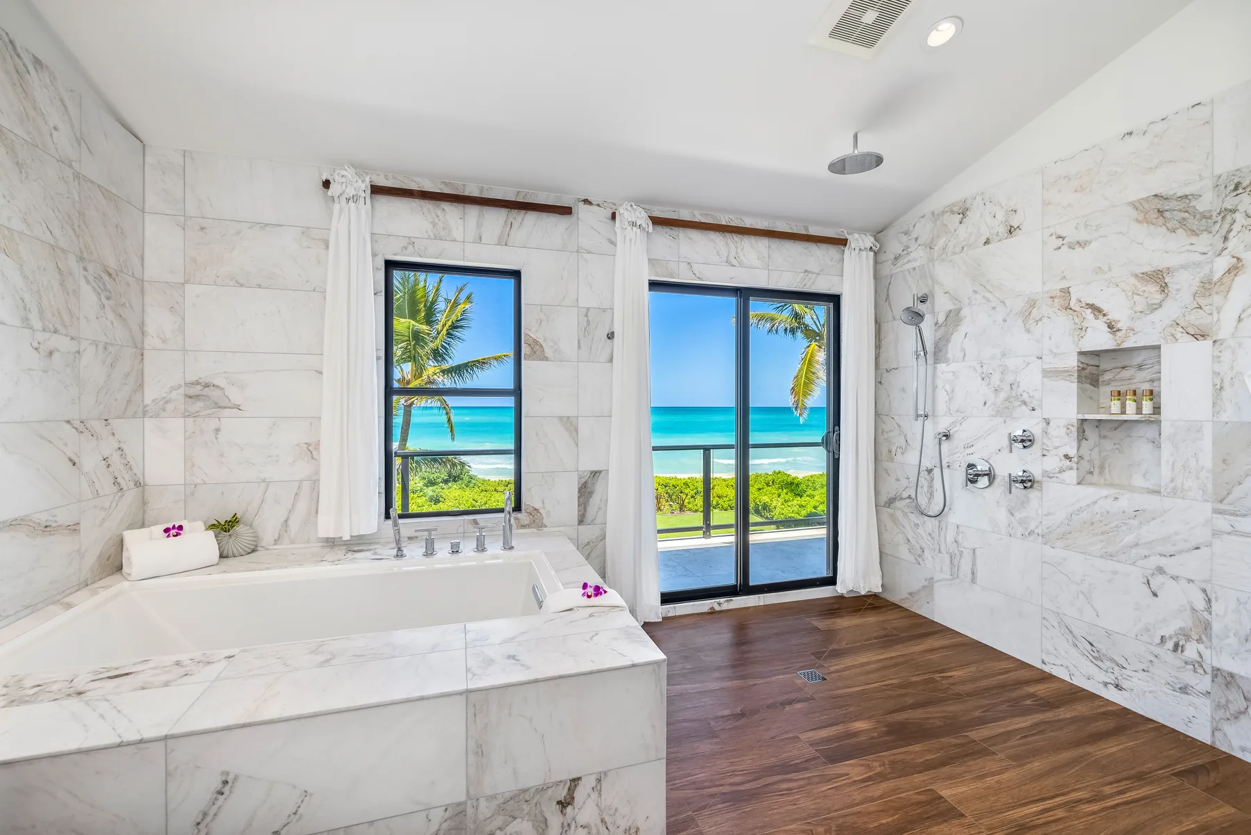 A bright bathroom with a built-in tub, glass doors, and ocean views.